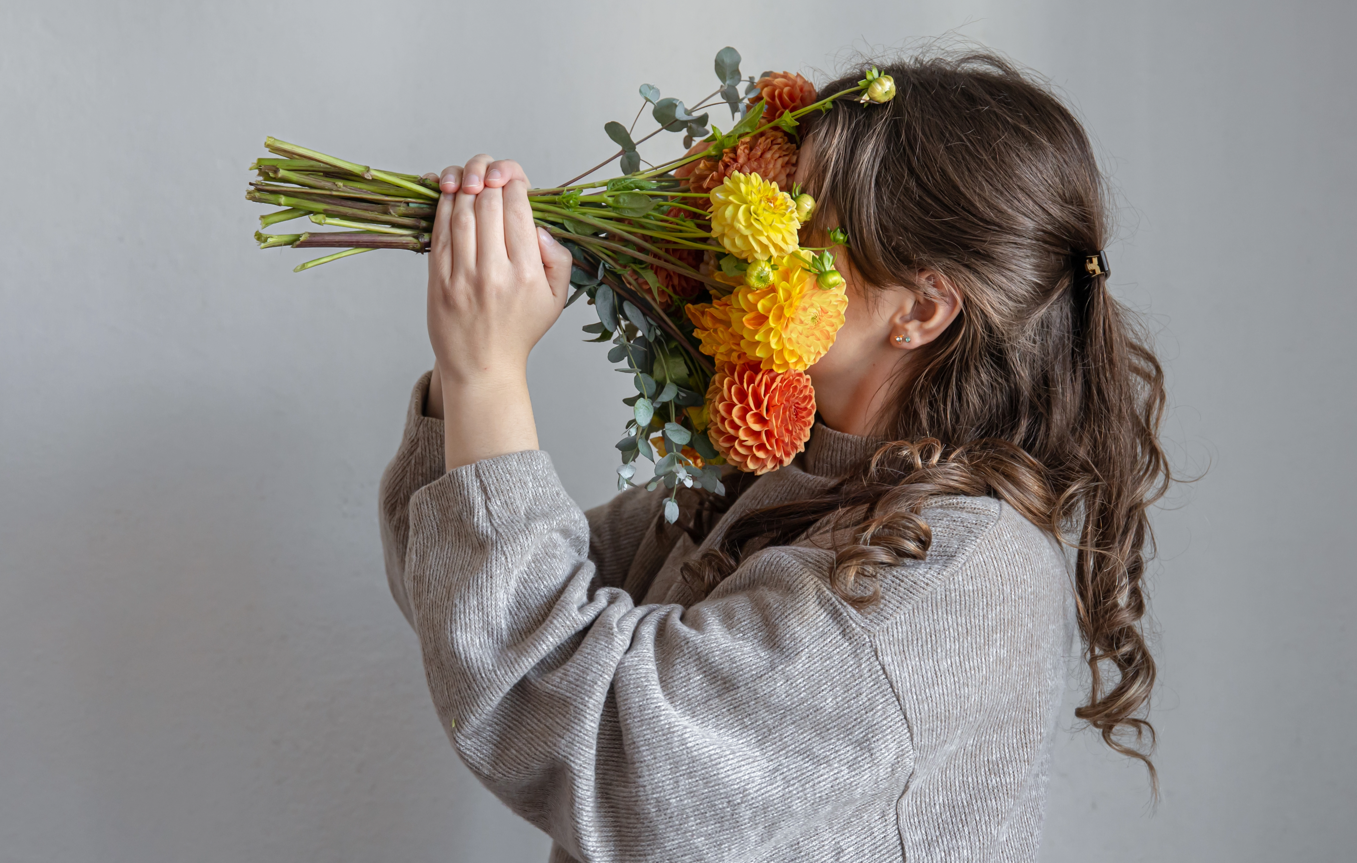 Lächelnde Frau versteckt ihr Gesicht hinter einem Blumenstrauß – Blumen verschenken mit Stil und Emotion